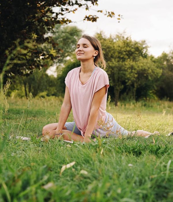 Woman sitting in a lotus pose practicing a breathing exercise in a serene environment.